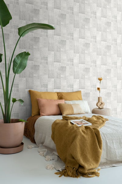 Schlafzimmer mit gemusterter Tapete, Bett, Kissen, Decken und Zimmerpflanze