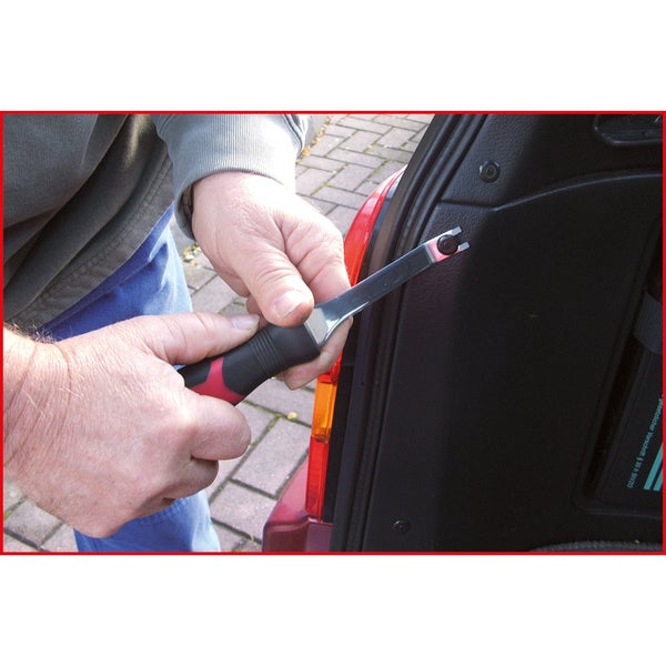 Eine Person entfernt mit einem Polsterkeil eine Befestigung im Kofferraum eines Autos.