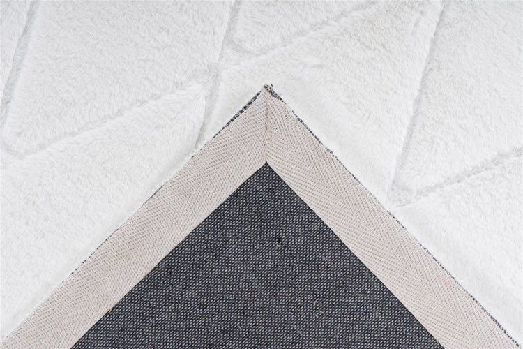 Detailansicht eines flauschigen Kunstfellteppichs mit geometrischem Muster und dessen gewebter Textilrückseite.