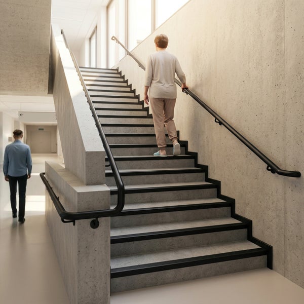 Modernes Treppenhaus mit Betontreppen, schwarzen Antirutschkanten und runden schwarzen Metallhandläufen an Betonwänden.