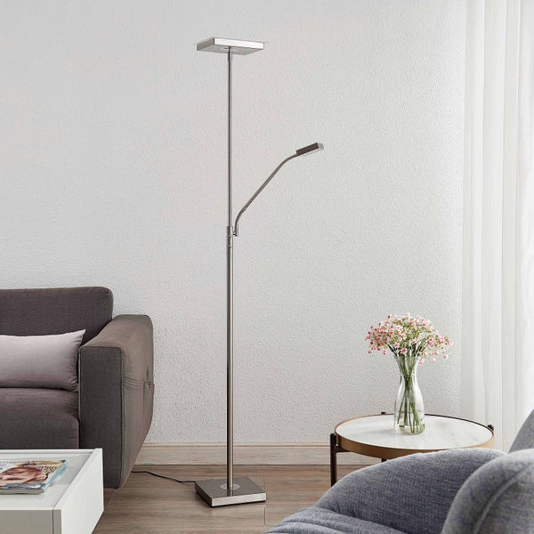 Moderne Stehleuchte aus Metall mit Deckenfluter und Lesearm in einem hellen Wohnzimmer neben einem Sofa und einem Beistelltisch.