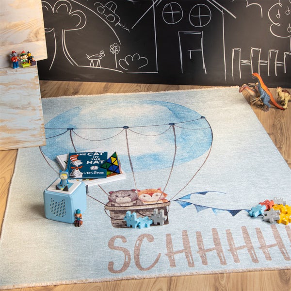 Ein Kinderteppich mit Heißluftballon Motiv zeigt einen Bären und einen Fuchs in einem Korb sowie den Schriftzug Schhhh in einem Kinderzimmer.
