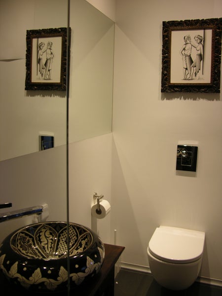 Badezimmer mit Spiegel, Waschbecken, Toilette und zwei gerahmten Bildern
