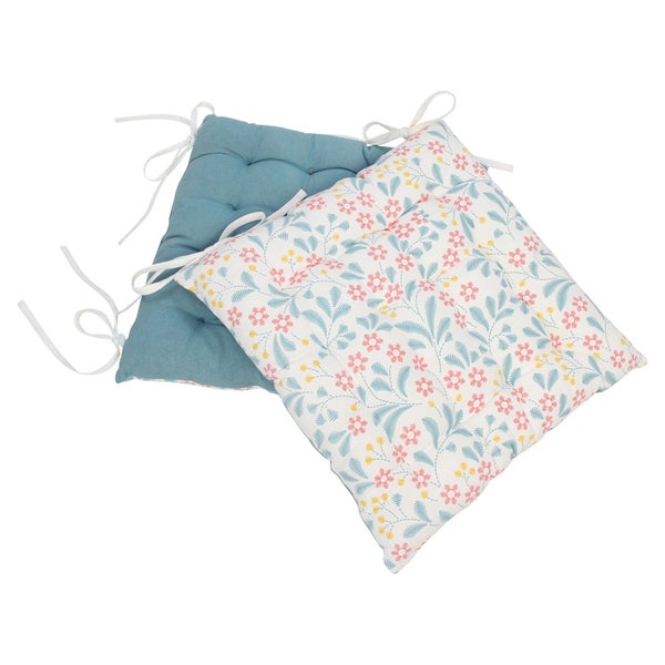 Zwei quadratische Stuhlkissen, eines in Petrol und eines mit Blumenmuster. Beide Sitzkissen haben eine Steppung und weiße Bindebänder.