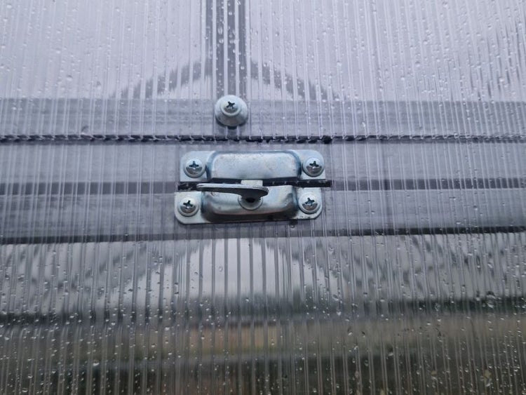 Detailaufnahme eines abschließbaren Fensterriegels an einem Gewächshaus