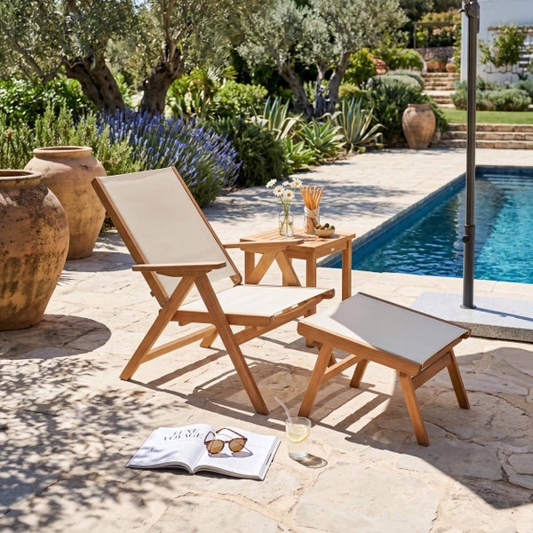 Holz-Deckchair mit Fußhocker und Beistelltisch auf heller Steinterrasse am Pool, umgeben von mediterranen Pflanzen und Terrakottatöpfen.