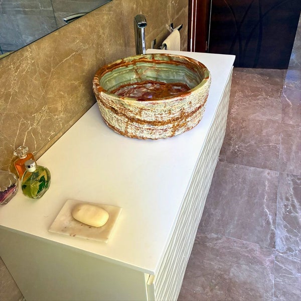Modernes Badezimmer mit rundem Naturstein-Aufsatzwaschbecken auf einem Unterschrank, verchromter Armatur und Wänden in Marmoroptik.