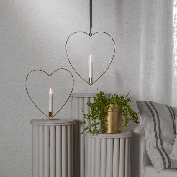 Dekorative Szene mit herzförmigen Kerzenhaltern auf Säulen und einer Zimmerpflanze