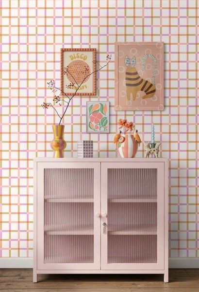 Wandgestaltung mit karo-gemusterter Tapete, rosa Sideboard mit geriffeltem Glas, Wandbildern und Dekorationsobjekten.