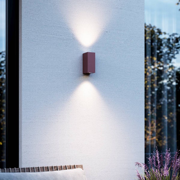 Rechteckige Außenwandleuchte in Rostoptik mit Lichtkegel nach oben und unten an einer verputzten Wand.