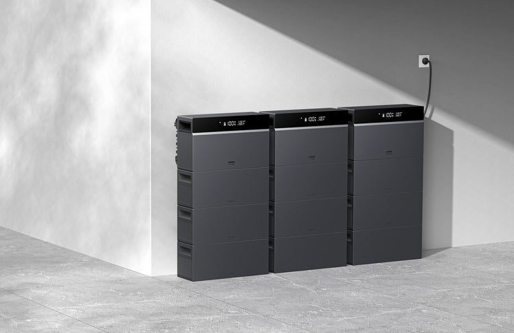 Drei Stapel modularer Heimspeicher in einem hellen Raum, eine Einheit an Steckdose angeschlossen, Statusanzeigen auf 100 Prozent.