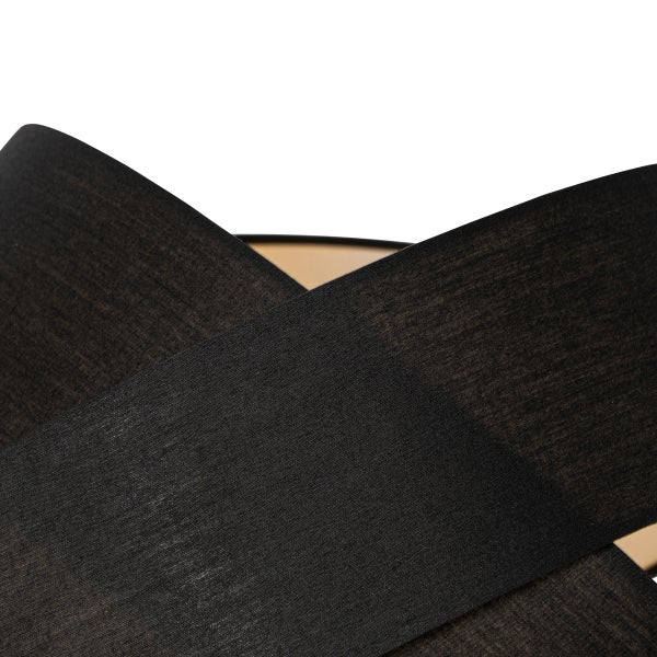 Detailansicht eines Lampenschirms mit überlappenden schwarzen Textilstreifen und goldfarbener Innenseite.