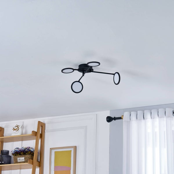 Moderne schwarze Deckenleuchte mit vier kreisförmigen LED-Elementen an schmalen Auslegern in einem hellen Wohnraum.