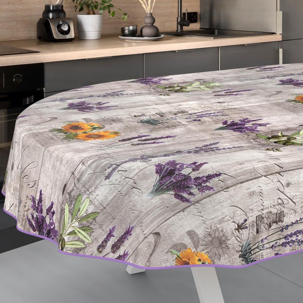 Ovale Tischdecke mit floralem Lavendel-, Sonnenblumen- und Olivenmuster auf Holzoptik in einer hellen, modernen Küche.