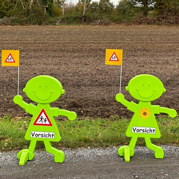 Zwei grüne Achtung Kinder Figuren mit Warnschildern stehen auf einem Weg