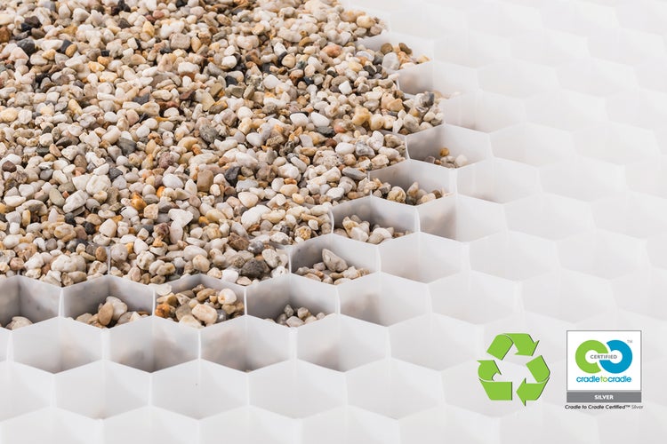 Kiesstabilisierungsgitter mit Wabenstruktur, teilweise gefüllt mit kleinem Kies. Mit Recycling-Symbol und Cradle to Cradle Silber Zertifizierung.