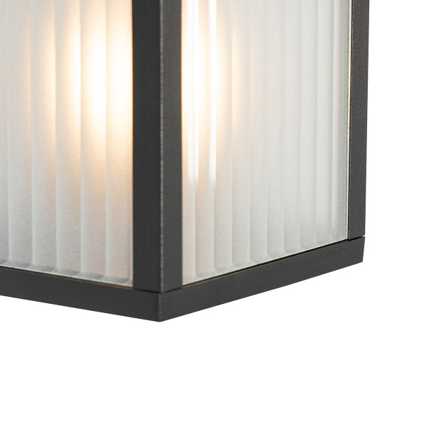 Nahaufnahme einer Leuchte mit schwarzem Metallrahmen und vertikal geriffeltem Glasdiffusor mit warmem Licht.