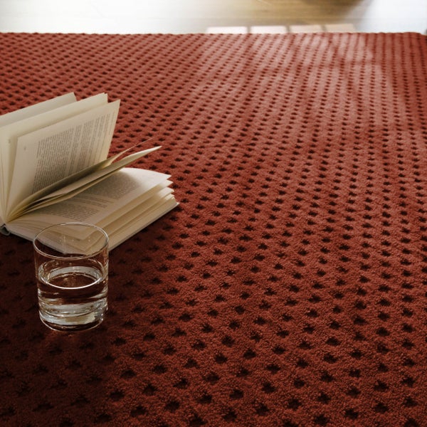 Roter strukturierter Teppich mit Waffelmuster, darauf ein Glas Wasser und ein aufgeschlagenes Buch.