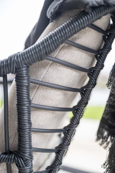 Nahaufnahme einer Gartenstuhl-Rückenlehne mit dunklem Geflecht und beigem Stoffkissen.