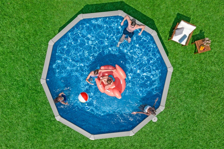 Achtseitiger Aufstellpool mit Personen, aufblasbarem Flamingo und Wasserball neben einer Gartenliege auf einer Rasenfläche.