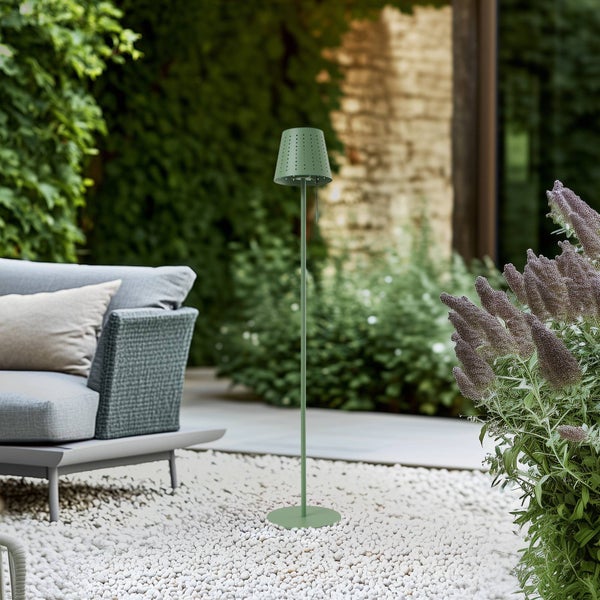 Grüne Stehleuchte für den Außenbereich mit perforiertem Lampenschirm auf einer Gartenterrasse mit weißen Steinen, Loungesessel und Pflanzen.
