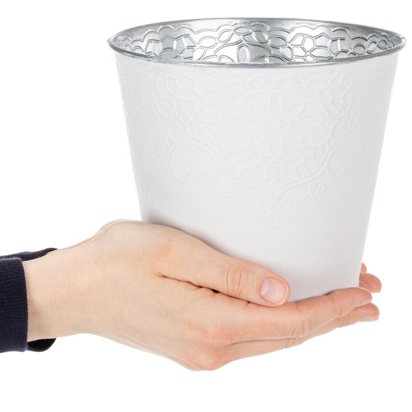 Metall-Übertopf in Weiß mit floraler Prägung, zur Größendarstellung in einer Hand gehalten.