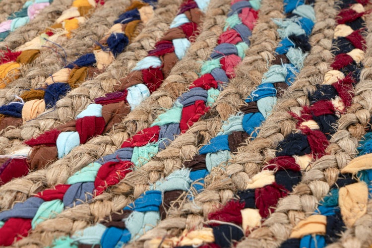 Runder geflochtener Teppich aus Jute mit bunten Textilresten in einem spiralförmigen Mosaikdesign.
