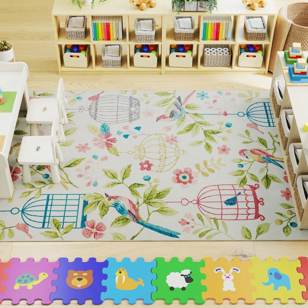 Helles Spielzimmer mit Kinderteppich mit Vogel-, Blumen- und Käfigmotiven, Regalen aus hellem Holz, weißen Holzstühlen und bunten Puzzlematten.
