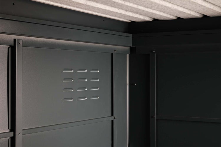 Innenansicht eines Metall-Gerätehauses mit Lüftungsschlitzen an der dunklen Wand und einer hellgrauen isolierten Decke.