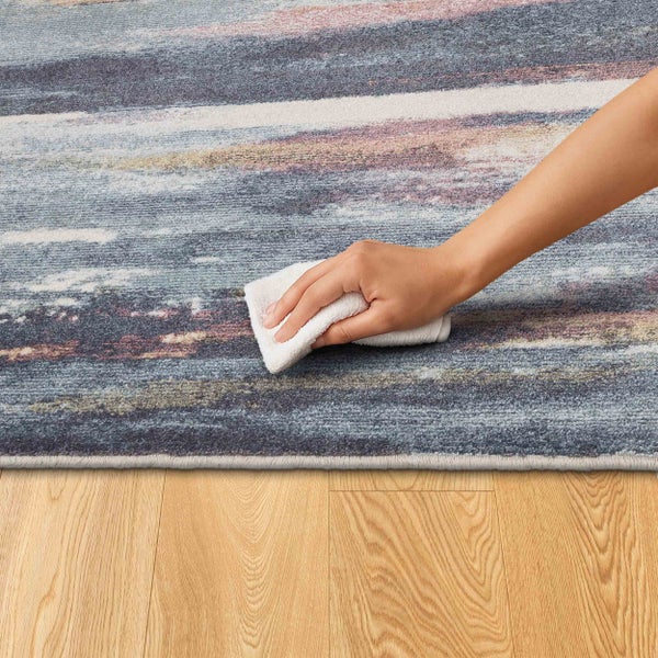 Eine Hand reinigt einen mehrfarbigen Teppich mit einem Tuch.