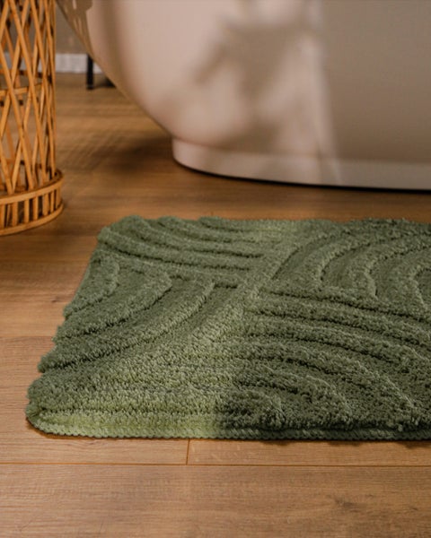Strukturierte Badmatte mit Wellenmuster auf Holzboden vor einer weißen Badewanne.