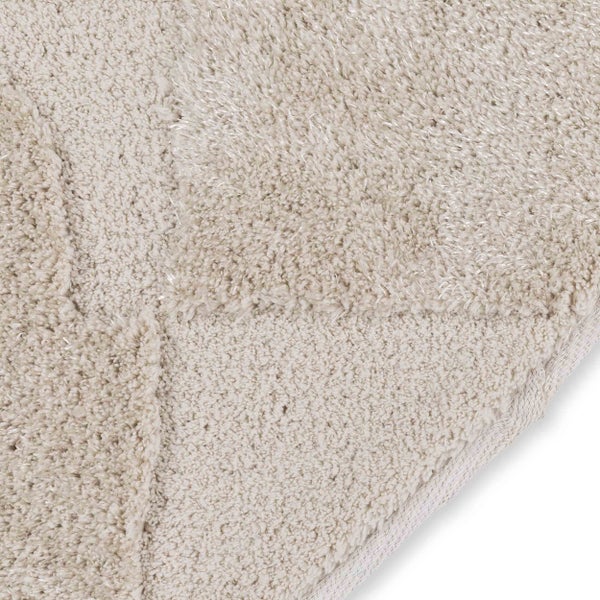 Detailaufnahme der weichen Textur eines Hochflor-Teppichs mit dezentem Muster und sauber verarbeitetem Rand.