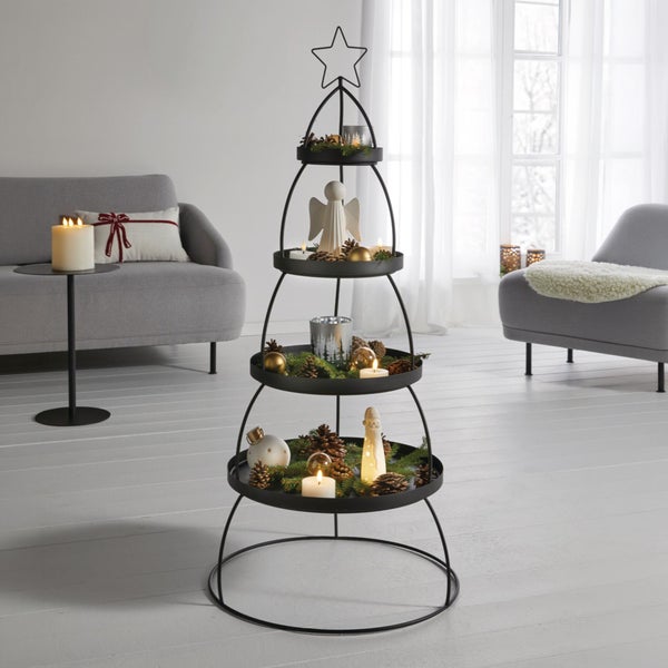 Weihnachtsbaum aus Metall mit drei Ablageebenen dekoriert mit Kerzen, Tannenzapfen und Dekofiguren in einem hellen Wohnzimmer.