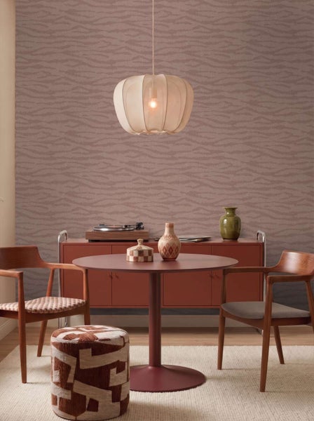 Wohnzimmer mit Vliestapete mit Wellenmuster, runder Esstisch, zwei Holzstühle, Hocker und Pendelleuchte vor einer texturierten Wand.