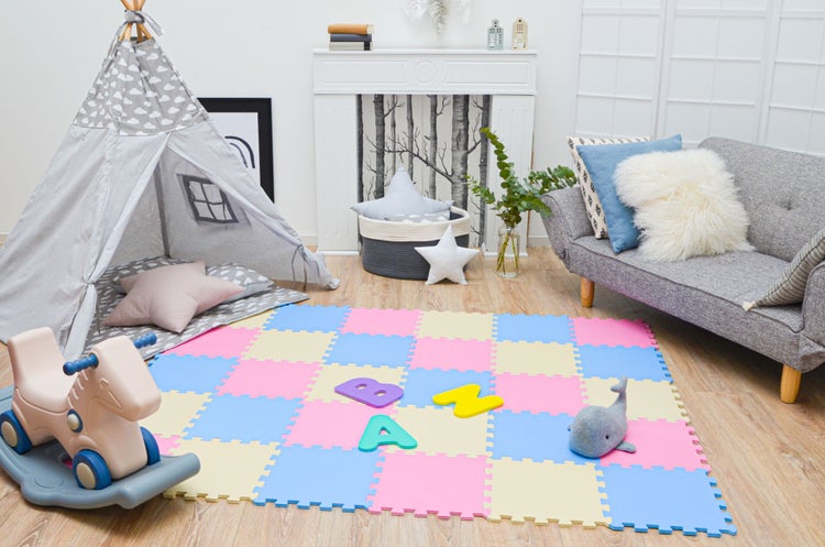 Hell eingerichteter Spielbereich mit buntem Puzzle-Spielteppich aus Schaumstoff, grauem Tipi-Zelt, Schaukelpferd und kleiner Couch.