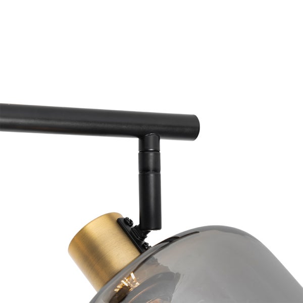 Nahaufnahme eines Deckenstrahlers mit schwarzem Metallarm, Fassung aus gebürstetem Messing und Schirm aus rauchgrauem Glas.
