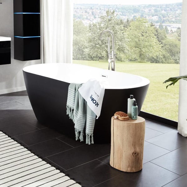 Freistehende Badewanne in einem modernen Badezimmer mit bodentiefem Fenster und Blick ins Grüne sowie einem Beistelltisch aus einem Baumstamm.
