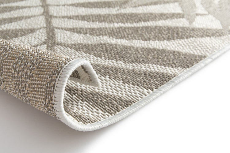 Detailaufnahme eines Flachgewebe-In- und Outdoor-Teppichs mit tropischem Blattmuster und geketteltem Rand.