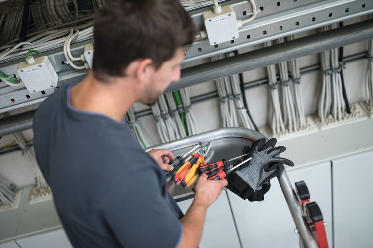 Elektriker auf einer Leiter mit Werkzeugen und Kabeln im Hintergrund