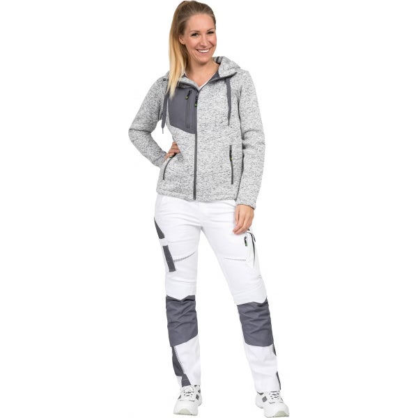 Frau in grauer Strickfleecejacke mit Kapuze und weißer Arbeitshose mit grauen Einsätzen.