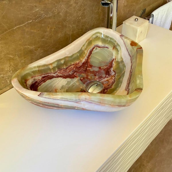 Helles Badezimmer mit einem organisch geformten Aufsatzwaschbecken aus Naturstein auf einem weißen Waschtisch vor einer Marmorwand.
