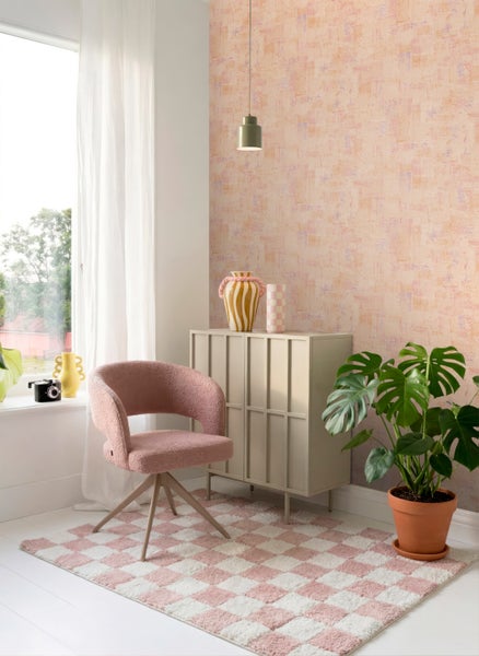 Helles Zimmer mit strukturierter Pastelltapete, beigem Schrank, rosa Drehstuhl, kariertem Teppich und einer Monstera-Pflanze.