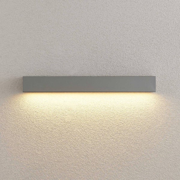Moderne rechteckige Wandleuchte in Dunkelgrau mit indirektem Lichtaustritt nach unten auf einer strukturierten Wand.