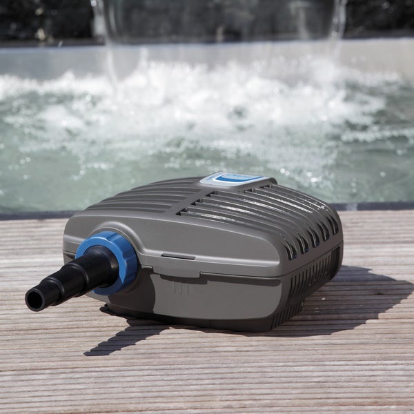 Graue Teichpumpe aus Kunststoff auf einer Holzterrasse vor einem fließenden Wasserfall im Garten.