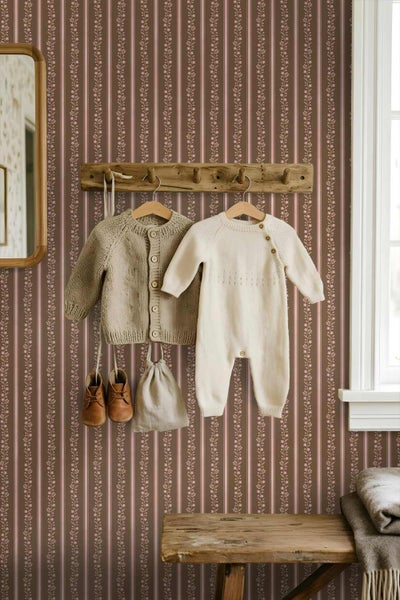 Vliestapete mit vertikalem Streifenmuster und floralen Ranken in einem hellen Kinderzimmer mit Holzelementen und Babykleidung.