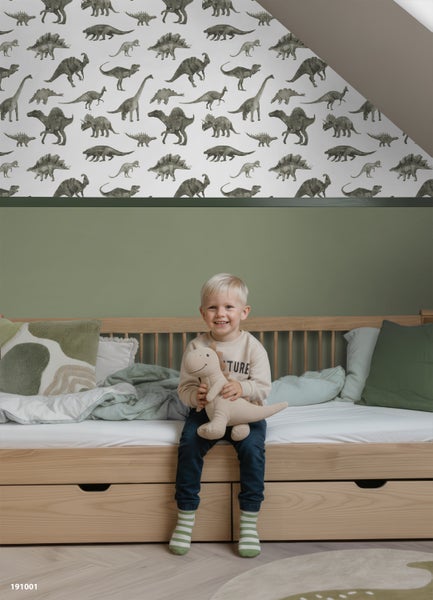Kinderzimmer mit einer Tapete mit Dinosaurier-Motiven über einer grünen Wand und einem Jungen auf einem Holzbett.