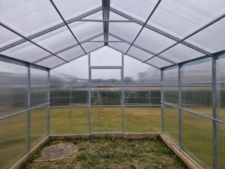 Innenansicht eines Gewächshauses mit Metallrahmen und Kunststoffplatten