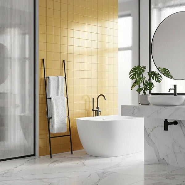 Modernes Badezimmer mit quadratischen Wandfliesen, freistehender Badewanne, Waschbecken auf Marmorplatte, Handtuchleiter und rundem Spiegel.