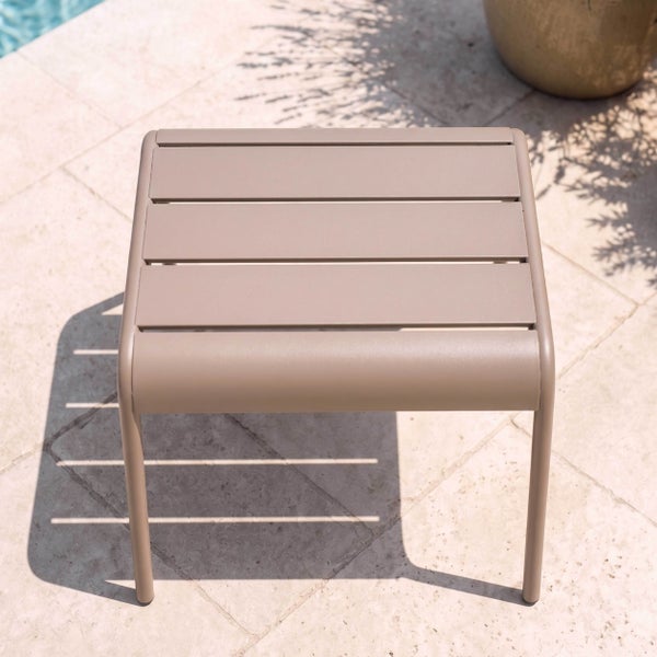 Moderner Gartenbeistelltisch aus Metall mit Lattenoberfläche auf einer hellen Steinterrasse an einem Pool.
