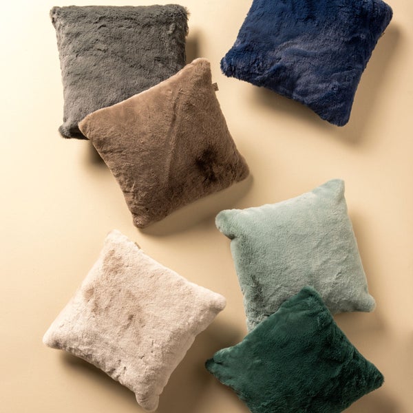 Mehrere quadratische Zierkissen mit Fellbezug in verschiedenen Farben liegen auf einem Untergrund